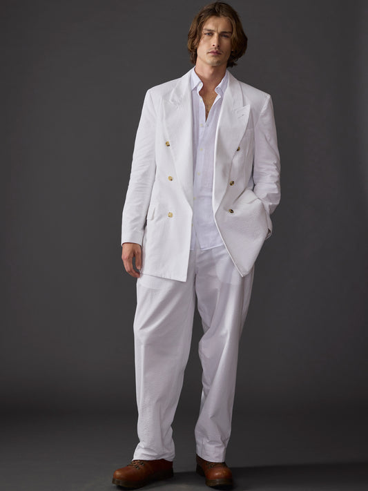 Model wearing a white seersucker suit styled with an open collar shirt against a dark background.