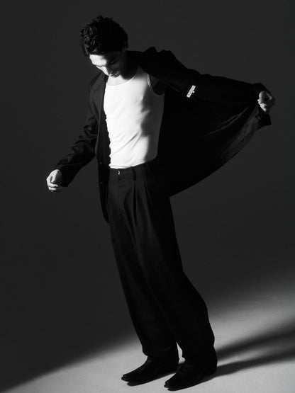 Black-and-white image of a man revealing the waistband and pleats of Lavelle chalk stripe trousers under a pulled-back jacket.