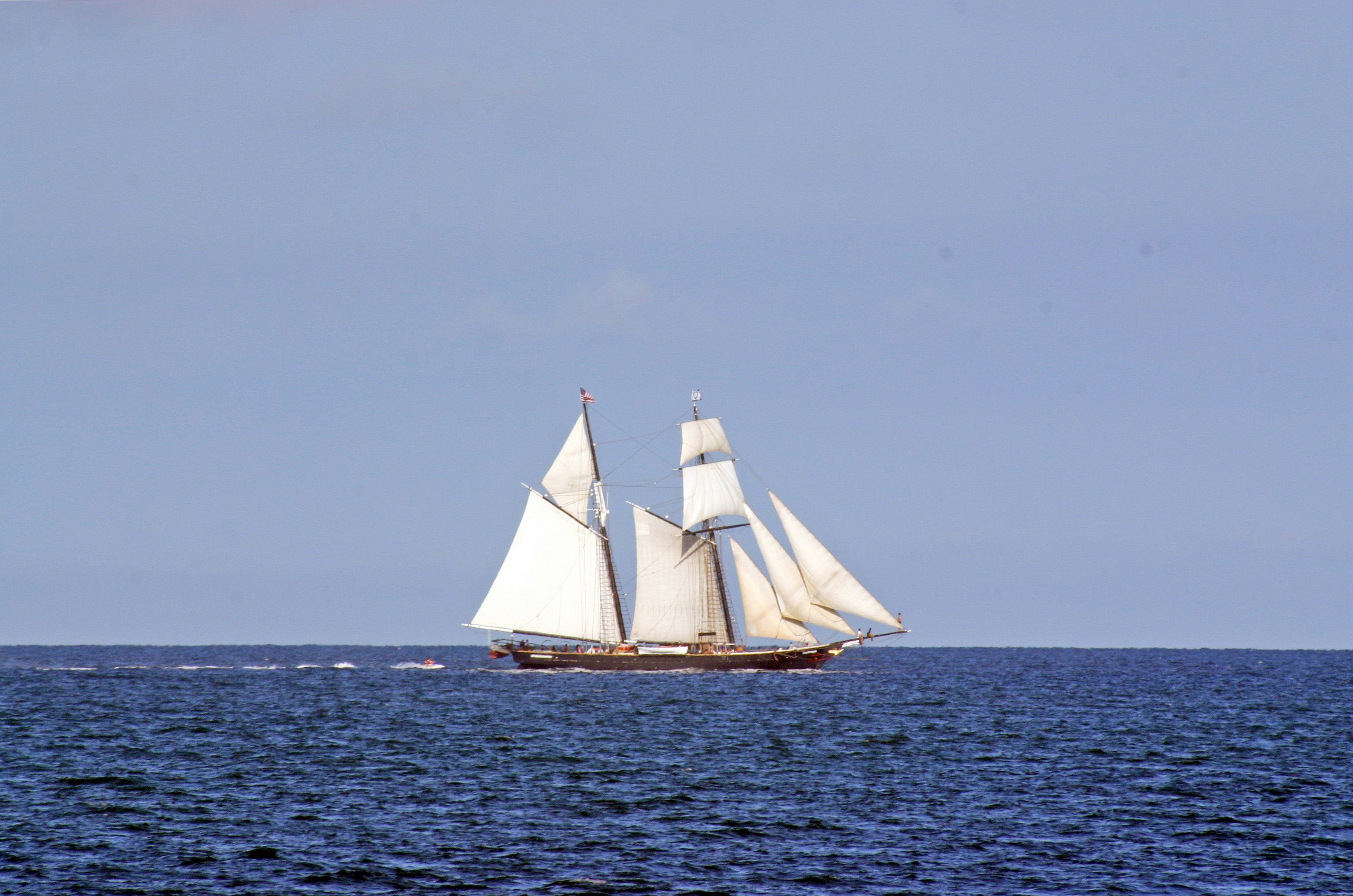 Film photo of a vintage ketch with eight white sails, sailing under a clear sky on a blue sea, capturing serene maritime scenery.